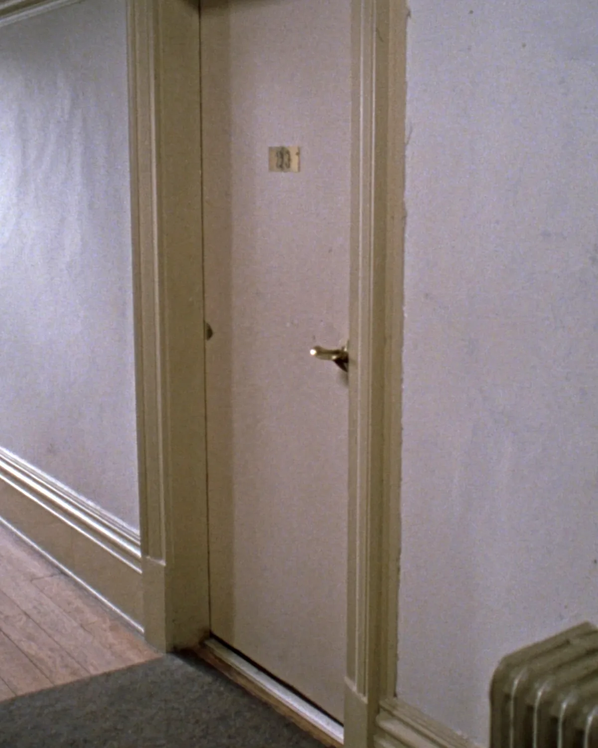A plain painted wooden door on an upstairs landing, closed, with a brass handle and a cast iron radiator beside it.
