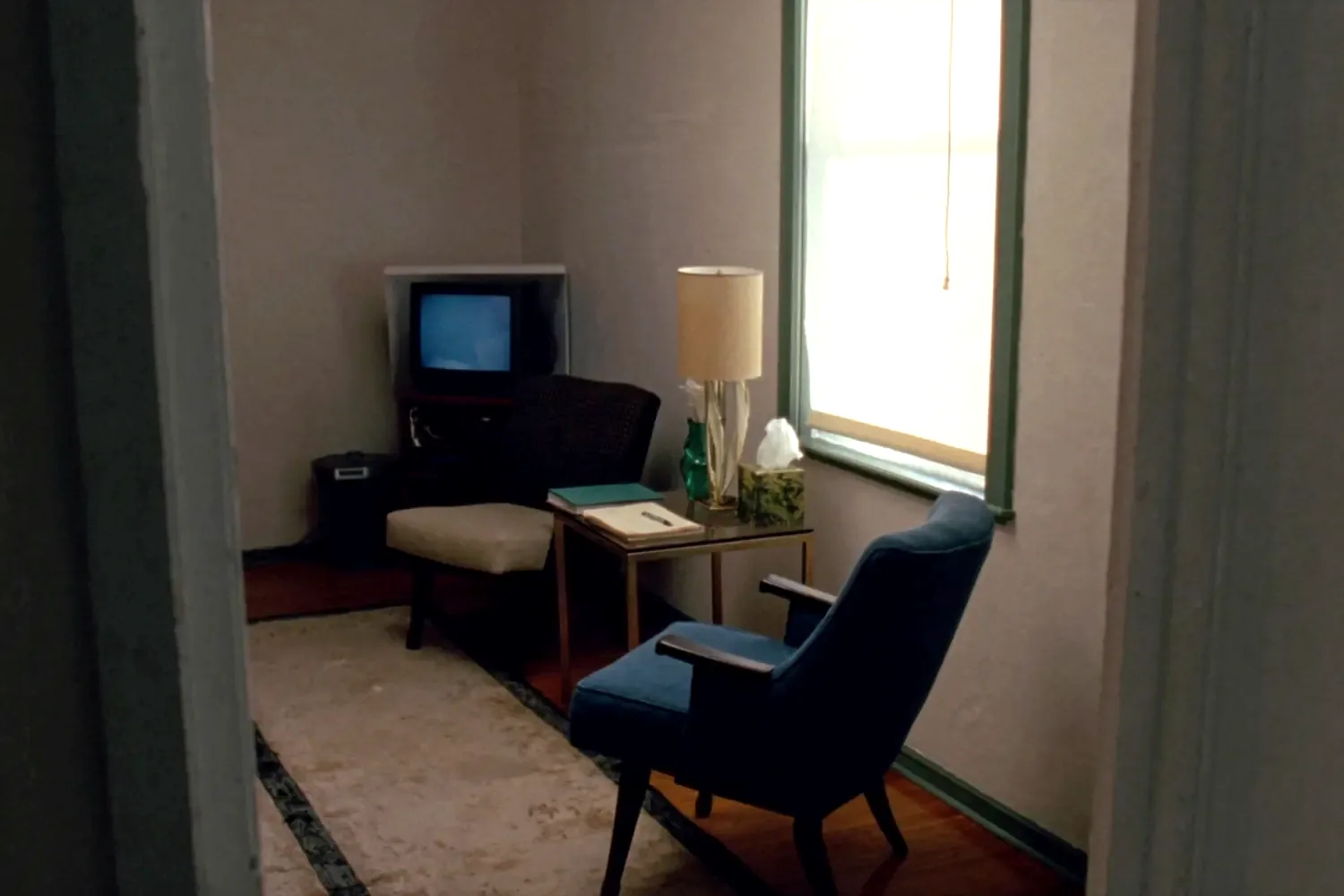 A small counselling room: two armchairs turned slightly toward each other, a lamp on a side table and a tall sash window.