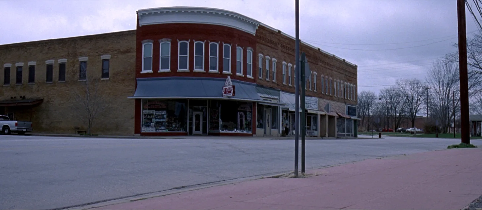 A quiet corner of a small Missouri main street, with two storey brick storefronts, wide empty pavement and an overcast sky.